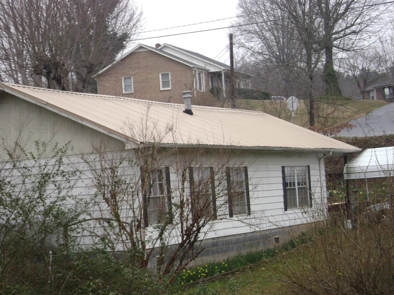 Tan metal roof on a white sided house set into a hillside — Commercial Roofing by Roofing Brothers in Lima